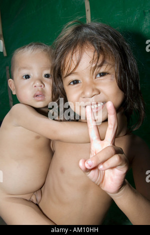 Girl holding her younger brother cheerily gives the victory salute, Phnom Penh, Cambodia Stock Photo