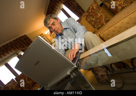 Middle aged man working on his laptop computer sitting on his sofa in the lounge of his house at home, UK Stock Photo