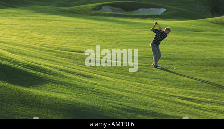 Man hitting iron shot off green fairway in low light
