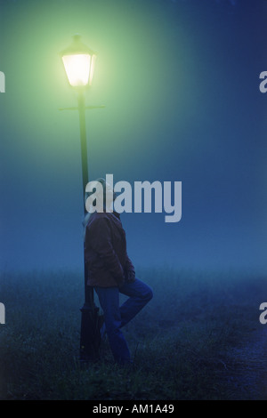 Woman leaning against lamp post on misty night Stock Photo