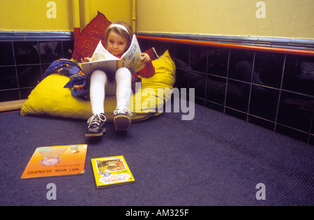 Girl reading book on big pillow in corner of classroom. Stock Photo