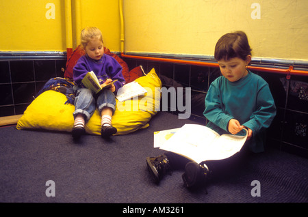 Girl and boy reading books on big pillows in corner of classroom. Stock Photo