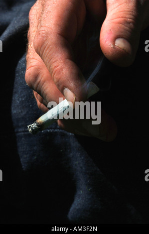 A Mans hand Holding An Unfiltered Rollup Lit Cigarette Stock Photo