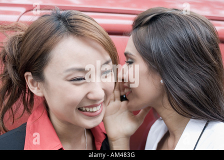 Close-up of a businesswoman whispering into an another businesswoman's ear and smiling Stock Photo