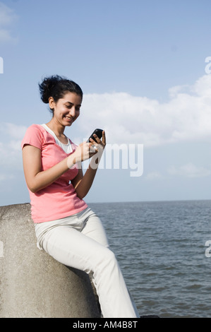 Young woman sitting on a rock and text messaging on a mobile phone Stock Photo
