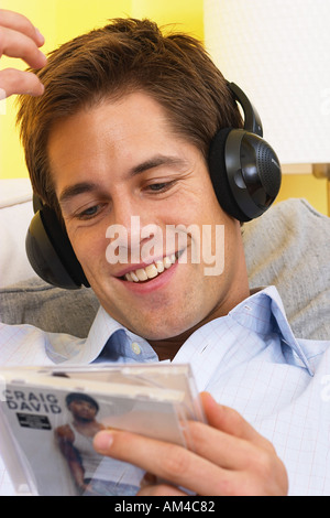 Man relaxing on sofa wearing headphones and holding compact disc  Stock Photo