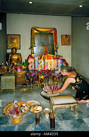 A pilgrim lights an incense stick in veneration of the mummified monk in the glass case at Wat Khunaram Koh Samui Thailand Stock Photo