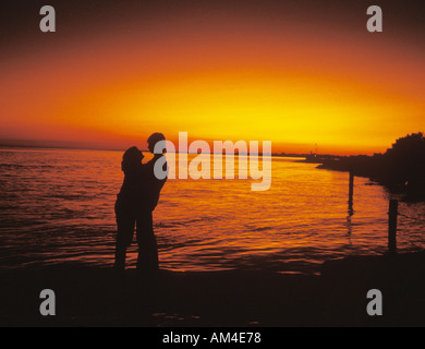 couple silhouetted by sunset on a dock at the ocean Stock Photo