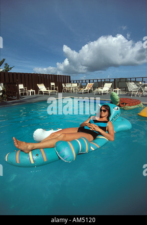 woman reclines in a pool float shaped like an alligator. Stock Photo