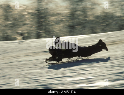 A boy rides on his fathers back while sleigh riding down a snowy hill Stock Photo