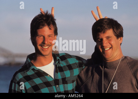 Two brothers pose for a photo and they both put fingers in a V shape up behind the head of the other Stock Photo