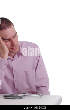 A young male doctor at his desk exhausted at the end of a long shift Stock Photo