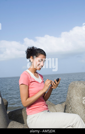 Side profile of a young woman sitting on a rock and text messaging on a mobile phone Stock Photo