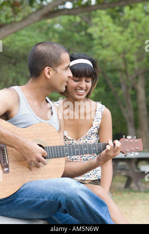 Young man sitting with his girlfriend and playing a guitar Stock Photo