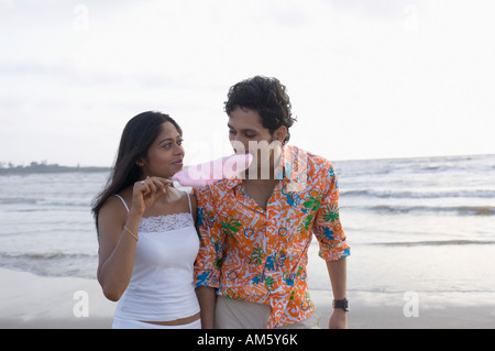 Young woman holding a cotton candy and a young man eating it Stock Photo