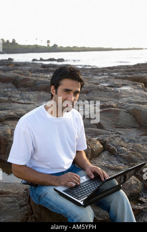 Portrait of a young man holding a laptop on his lap and smiling, Madh Island, Mumbai, Maharashtra, India Stock Photo