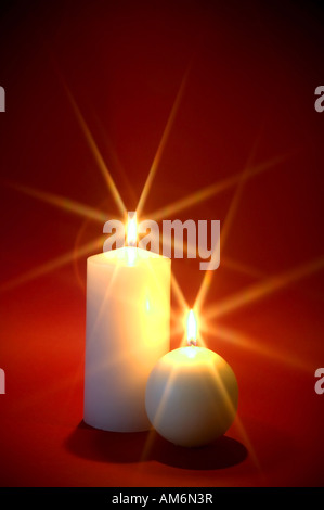 Two white candles burning against a red background Christmas theme Stock Photo