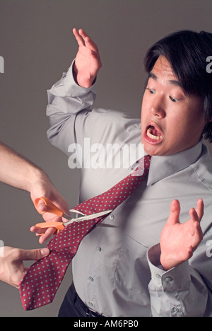 Scissors cutting tie of shocked Asian businessman Stock Photo