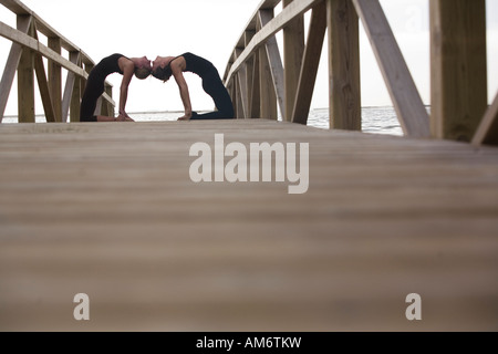 two women practise yoga poses on wood deck in nature Stock Photo