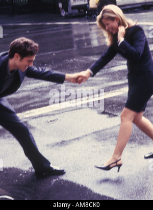 Young man holding woman's hand on wet road Stock Photo