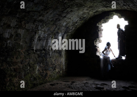 A gothic male and female couple in an old ruined stone walled window within a cellar type roon at Dunnottar castle, Scotland. Stock Photo