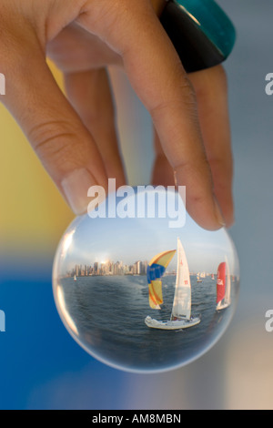 sailboat in a glass, a woman holding a sphere with a sailboat behind refracting in the glass Stock Photo