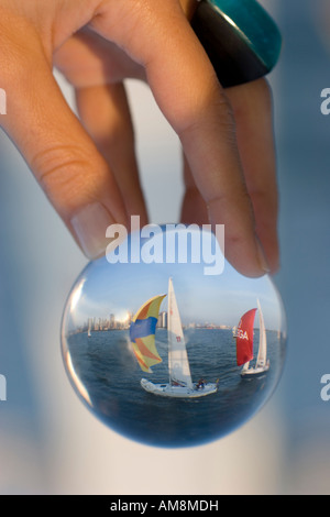 sailboat in a glass, a woman holding a sphere with a sailboat behind refracting in the glass Stock Photo