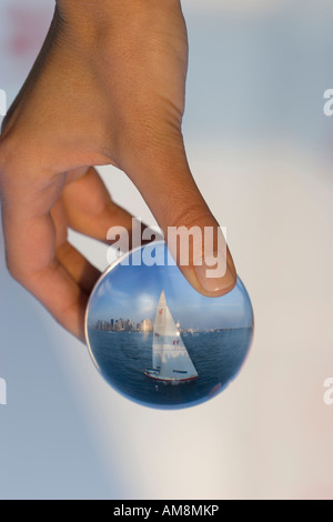 sailboat in a glass, a woman holding a sphere with a sailboat behind refracting in the glass Stock Photo