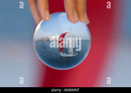 sailboat in a glass, a woman holding a sphere with a sailboat behind refracting in the glass Stock Photo