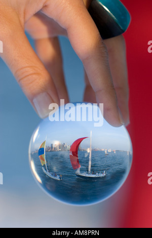 sailboat in a glass, a woman holding a sphere with a sailboat behind refracting in the glass Stock Photo