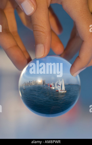 sailboat in a glass, a woman holding a sphere with a sailboat behind refracting in the glass Stock Photo