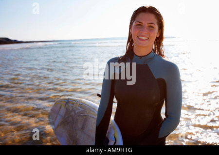 Woman standing on beach with surfboard smiling. Stock Photo