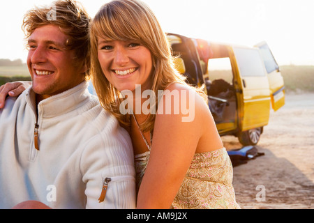 Couple sitting on beach smiling with van in background. Stock Photo