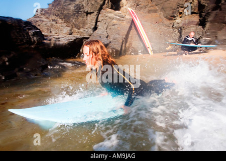 Woman on surfboard smiling with man in background with surfboard. Stock Photo