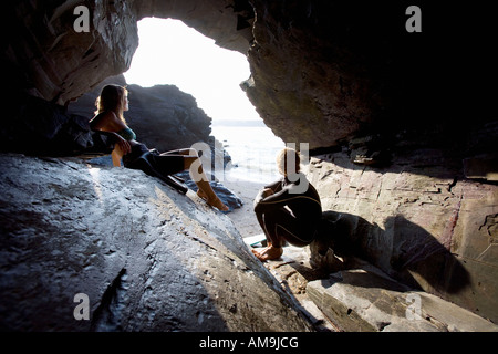 Couple sitting on large rocks in wetsuits. Stock Photo