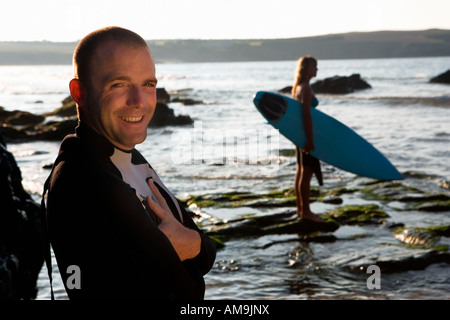 Man standing smiling with woman holding surfboard in background. Stock Photo
