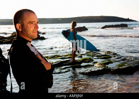 Man standing smiling with woman holding surfboard in background. Stock Photo