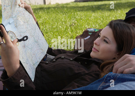 Woman smiling holding map reclining on sleeping man in a park. Stock Photo