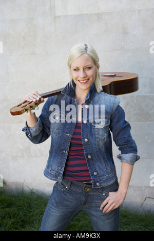 Woman standing holding a guitar smiling.