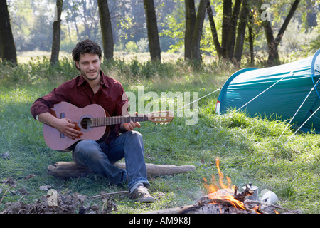 Man at campsite playing guitar and smiling. Stock Photo
