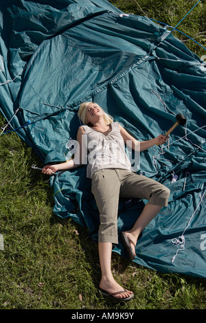 Woman holding mallet lying on tent smiling. Stock Photo