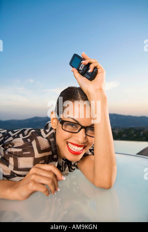 Woman leaning on table holding cellular phone smiling outdoors. Stock Photo