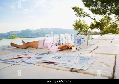 Woman lying by infinity pool with newspaper over her face. Stock Photo