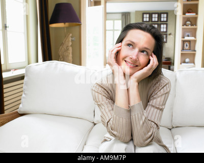 Woman sitting on sofa in living room smiling. Stock Photo