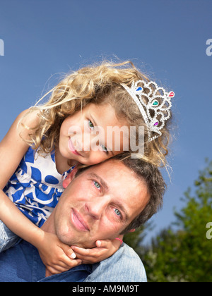 Man with smiling young girl wearing tiara on shoulders. Stock Photo