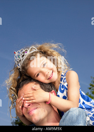 Man with smiling young girl wearing tiara on shoulders. Stock Photo