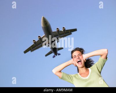 Woman covering ears and screaming with plane flying overhead. Stock Photo