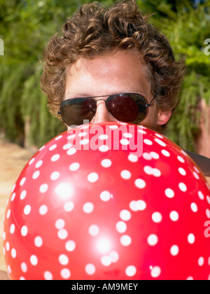 Man blowing up a balloon and wearing sunglasses. Stock Photo