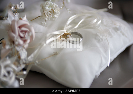 A close up portrait of a wedding ring  tied to a white ribbon on a white cushion Stock Photo