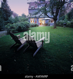 Two lawn chairs sitting on a lawn with a large house in the background. Stock Photo